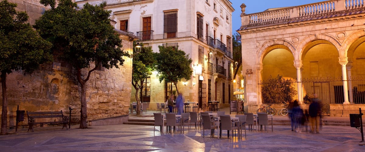 A historic square with stone buildings, outdoor seating, and an ornate archway.