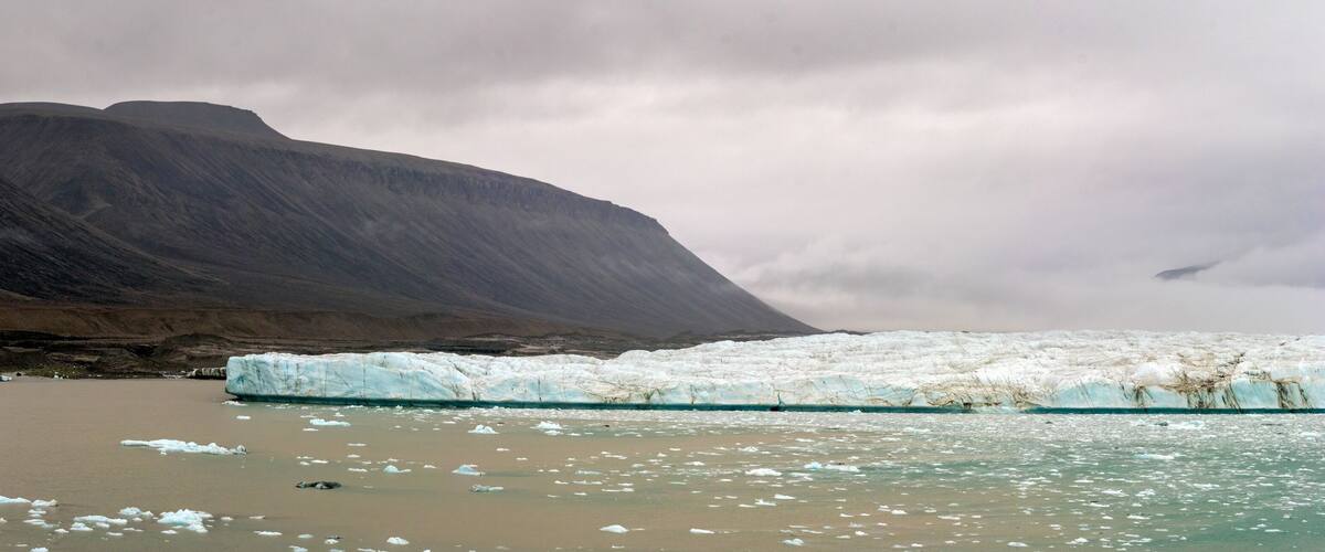 A glacier in a mountainous area with a large ice formation in the foreground and a mountain in the background.