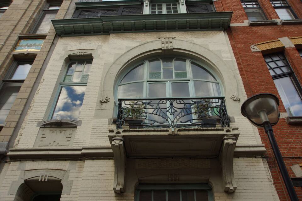 A building with a large arched window, a balcony with ornate metalwork, and a street lamp.