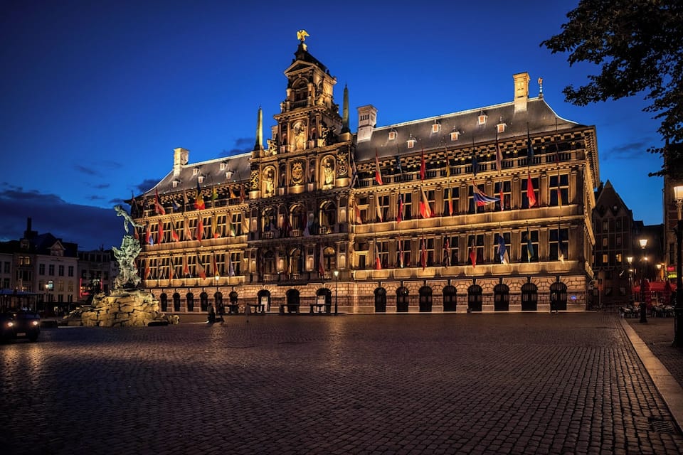 A historic building with ornate architecture, a prominent clock tower, and a statue in the foreground.