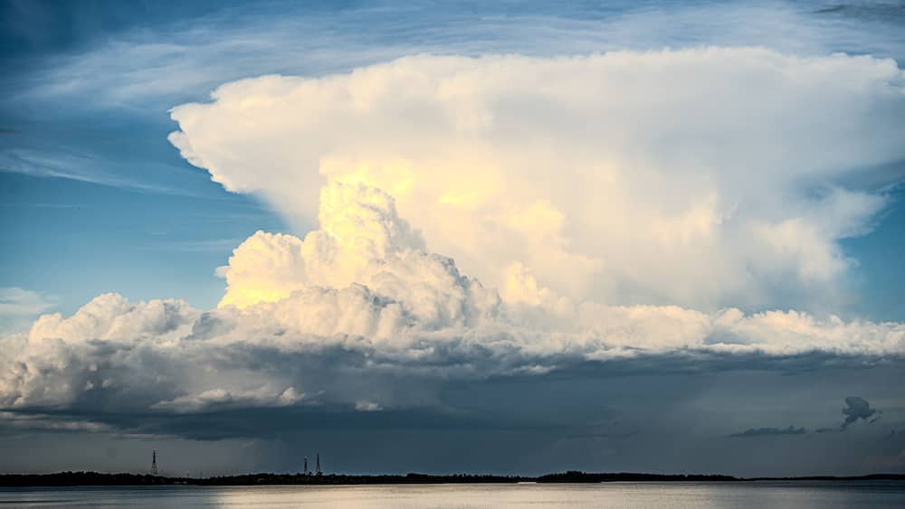Eine große Wolkenformation über einem Gewässer bei blauem Himmel.
