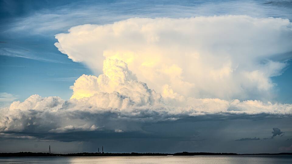 A large cloud formation over a body of water with a clear sky.