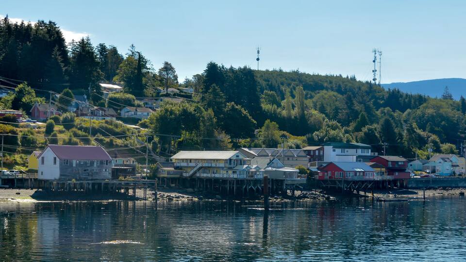 A coastal village with houses on stilts by the water, surrounded by dense forest and hills.