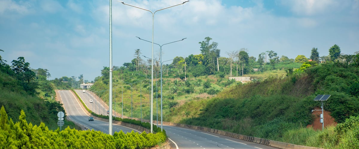 A curved highway with streetlights, surrounded by lush greenery and hills.