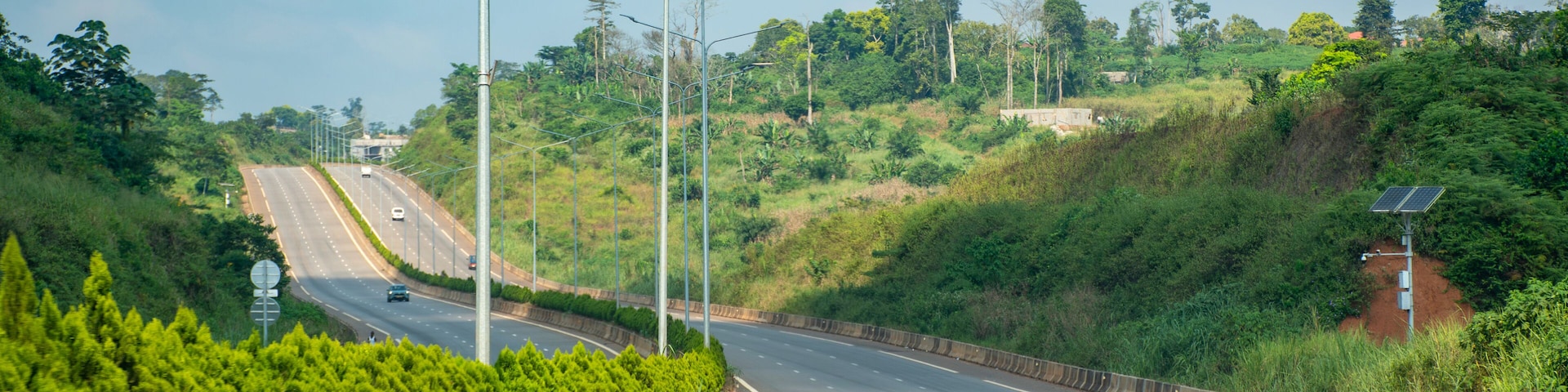 A curved highway with streetlights, surrounded by lush greenery and hills.