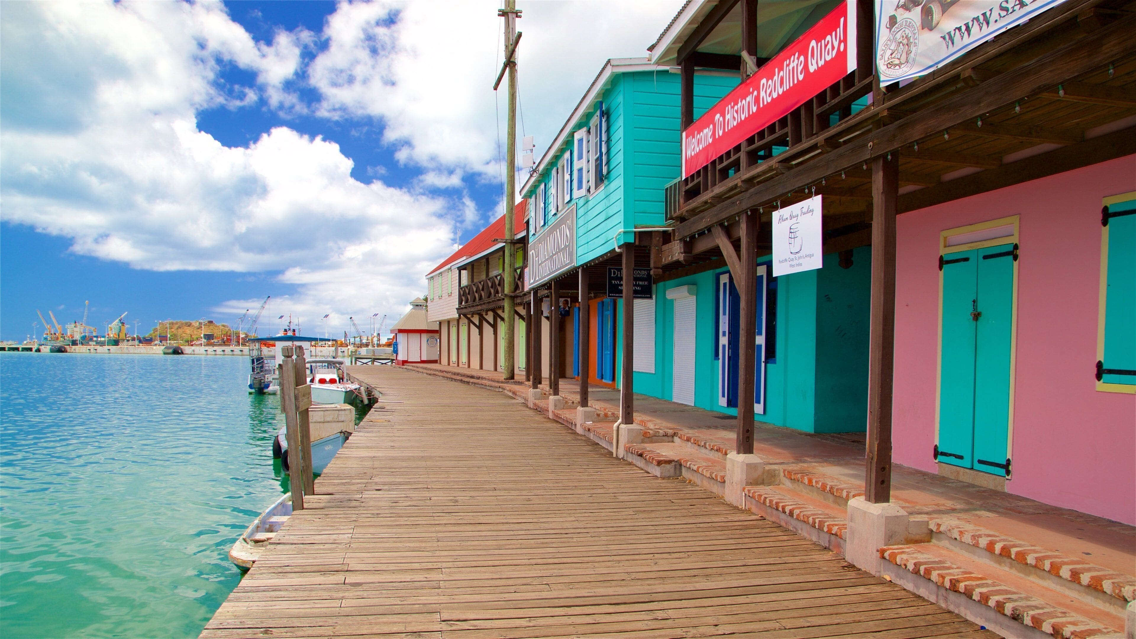 Un muelle de madera se adentra en aguas turquesas, bordeado por edificios coloridos, incluyendo un letrero rojo que da la bienvenida a Historic Redcliffe Quay.
