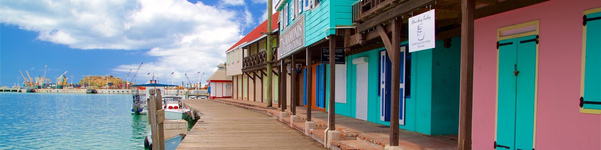 Un muelle de madera se adentra en aguas turquesas, bordeado por edificios coloridos, incluyendo un letrero rojo que da la bienvenida a Historic Redcliffe Quay.