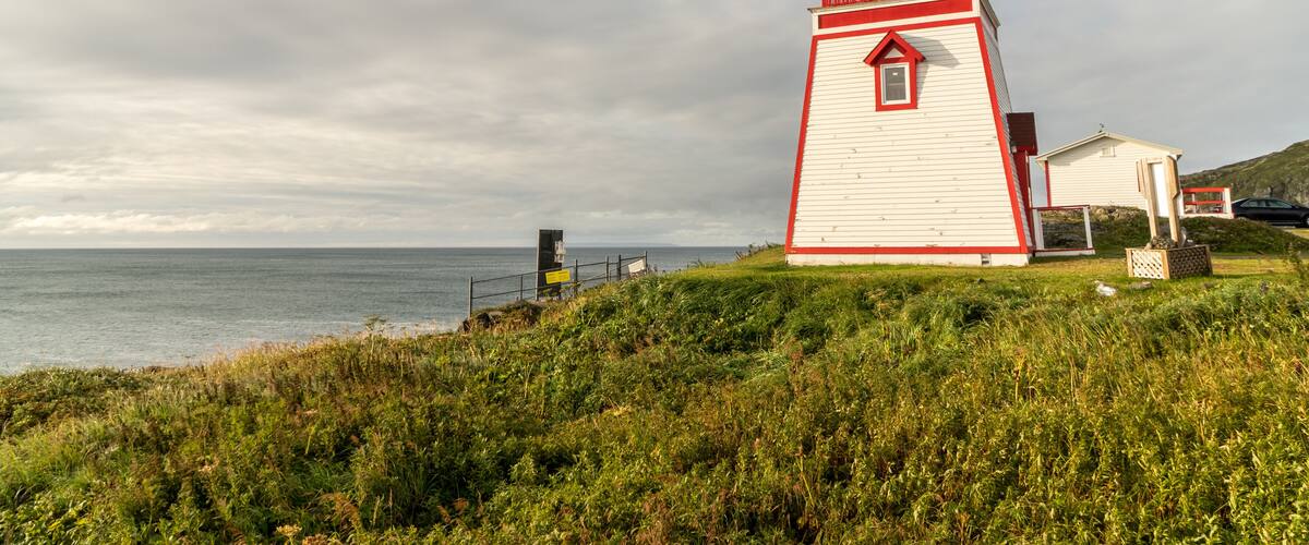 Un phare blanc et rouge au bord de la mer, avec un premier plan herbeux et un ciel nuageux.