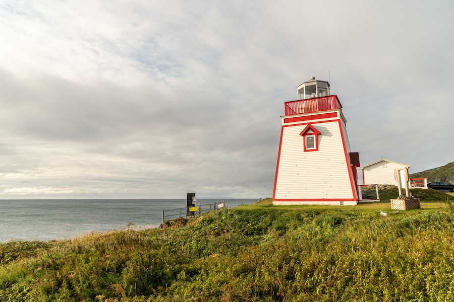 Un phare blanc et rouge au bord de la mer, avec un premier plan herbeux et un ciel nuageux.