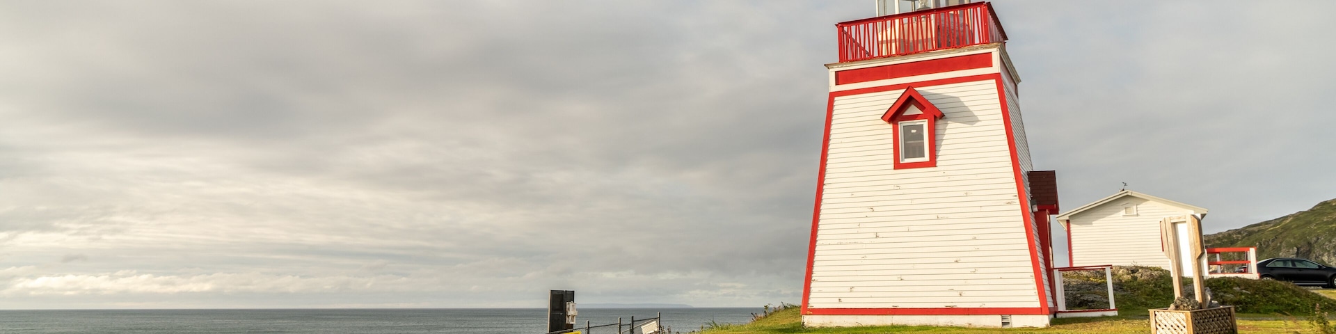 Um farol branco e vermelho à beira-mar, com grama na frente e céu nublado.