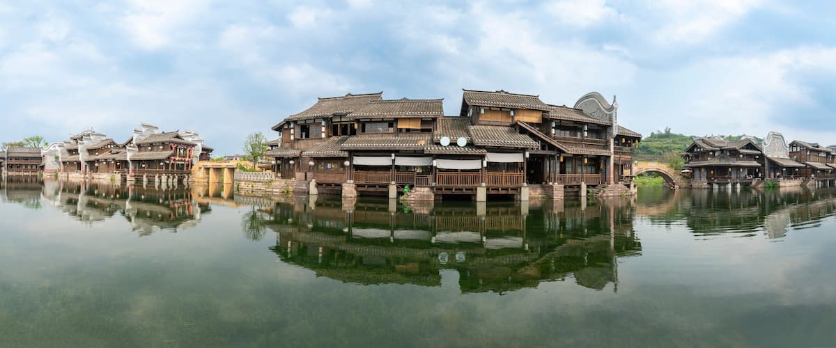 Traditional wooden buildings with tiled roofs reflecting on a calm body of water.