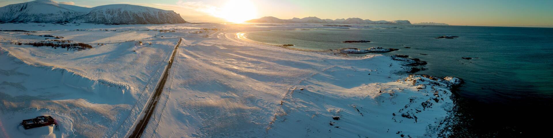 A snowy landscape with a frozen sea, a clear sky, and a sunset.