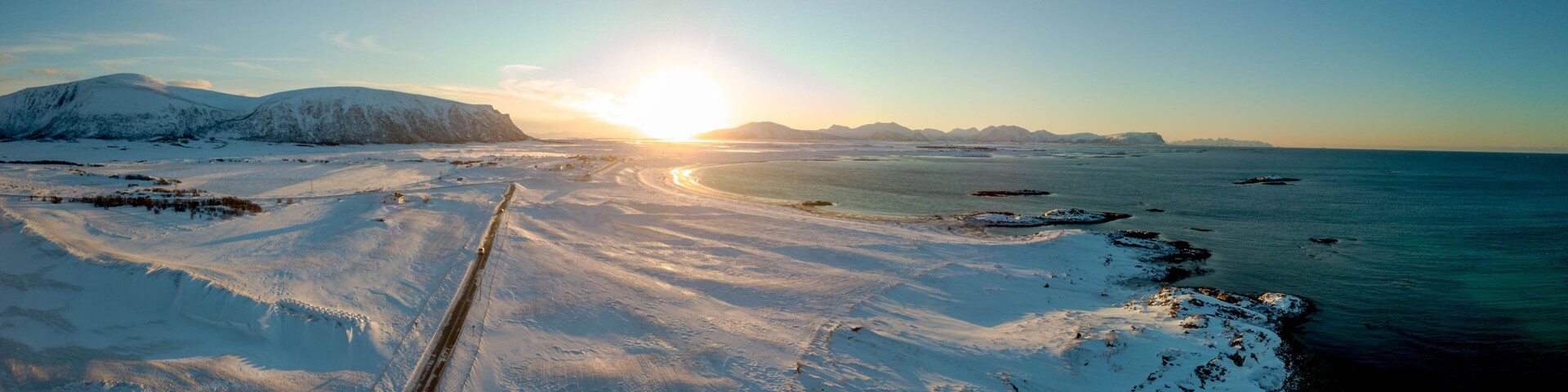 Paisagem nevada com mar congelado, céu claro e pôr do sol.