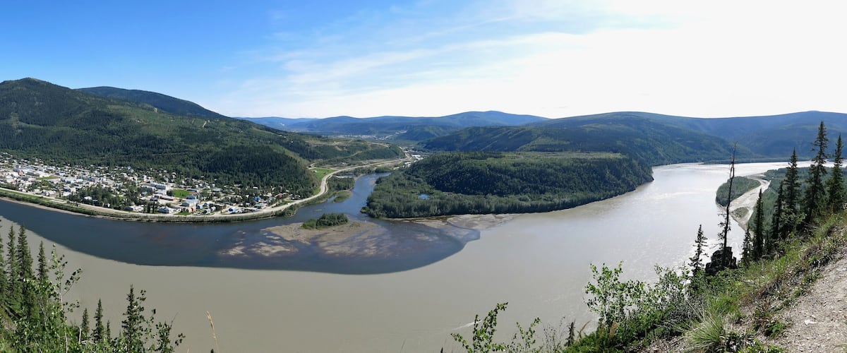 A river winding through a valley with a town on one side and mountains in the background.