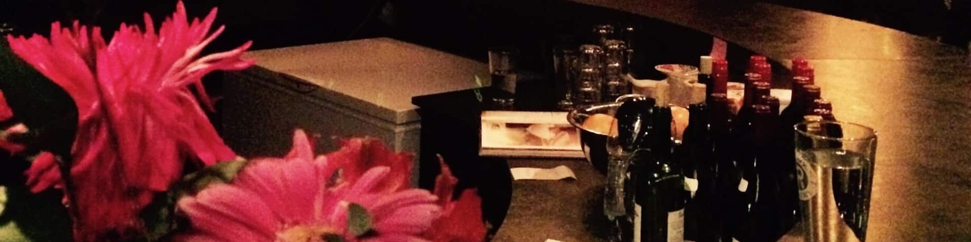 A dimly lit bar with a chandelier, framed pictures on the wall, and a bar counter with bottles and glasses.