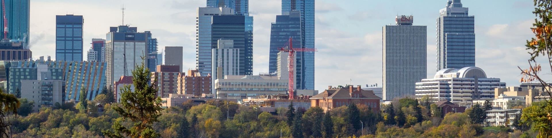 A city skyline with modern skyscrapers, surrounded by autumn foliage and a clear blue sky.