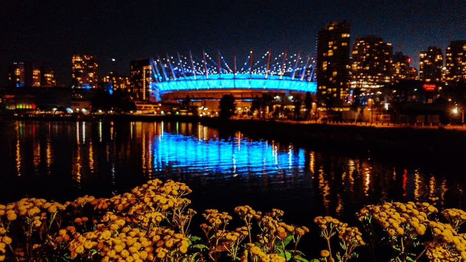 A city skyline at night with a brightly lit bridge reflecting on the water.