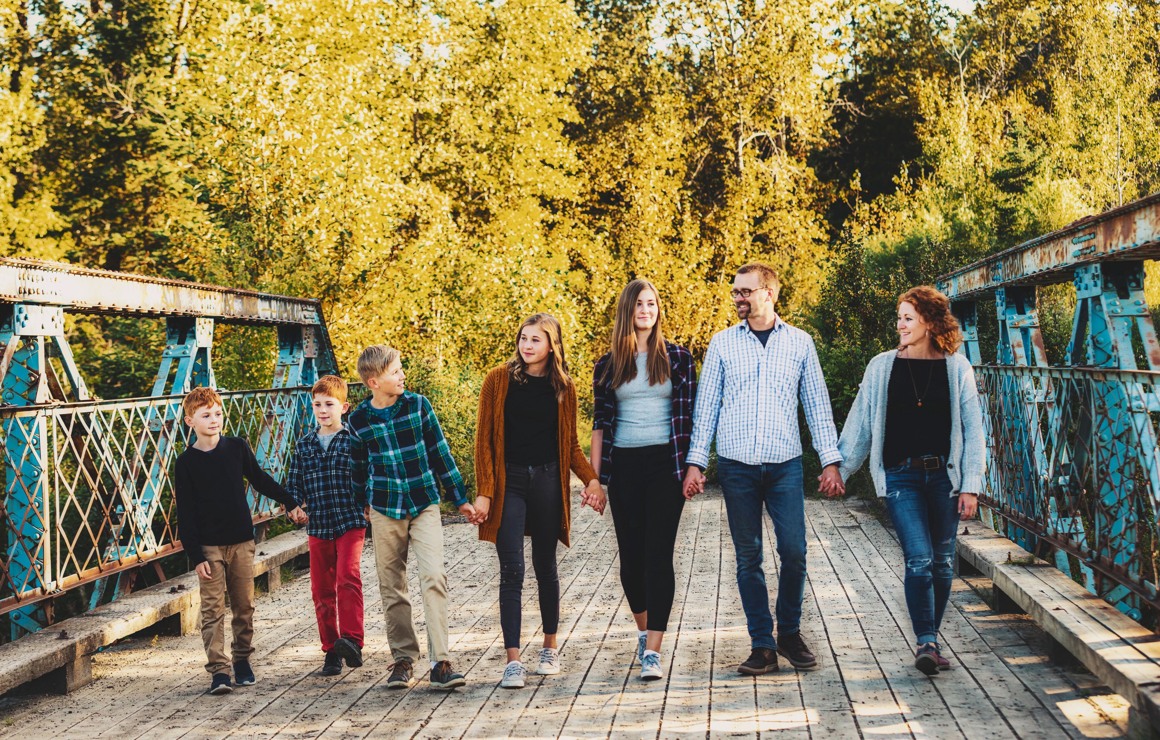 Family of seven walking in a row and holding hands as they walk across a bridge in a city park in autumn; Edmonton, Alberta, Canada