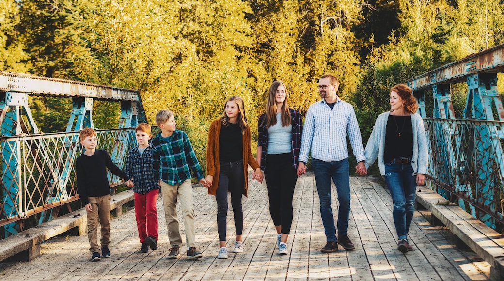 Family of seven walking in a row and holding hands as they walk across a bridge in a city park in autumn; Edmonton, Alberta, Canada