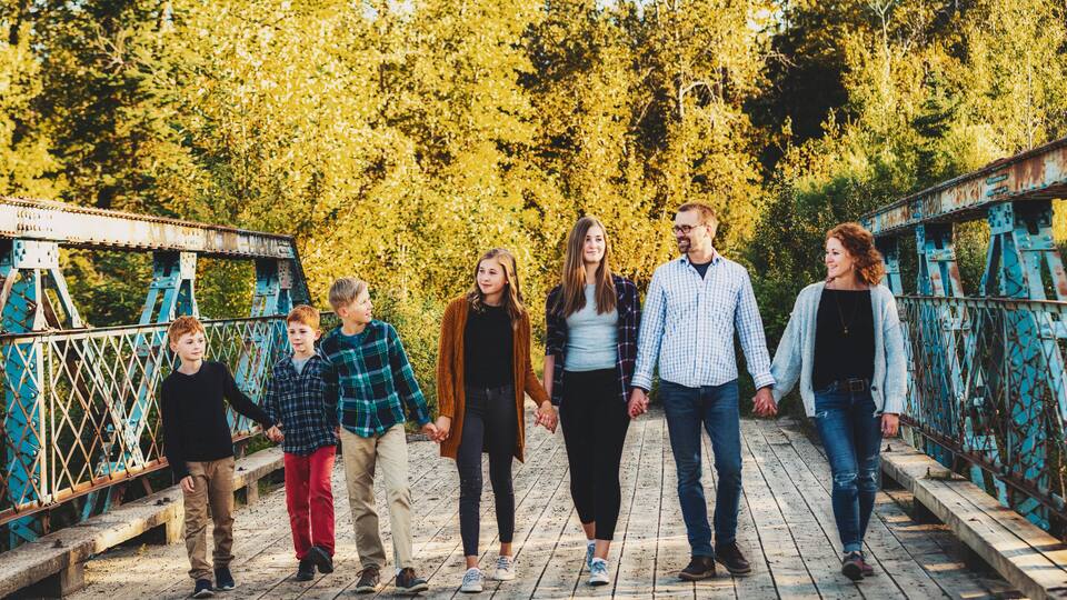 A group of people walking on a wooden bridge with metal railings, surrounded by trees with yellow leaves.