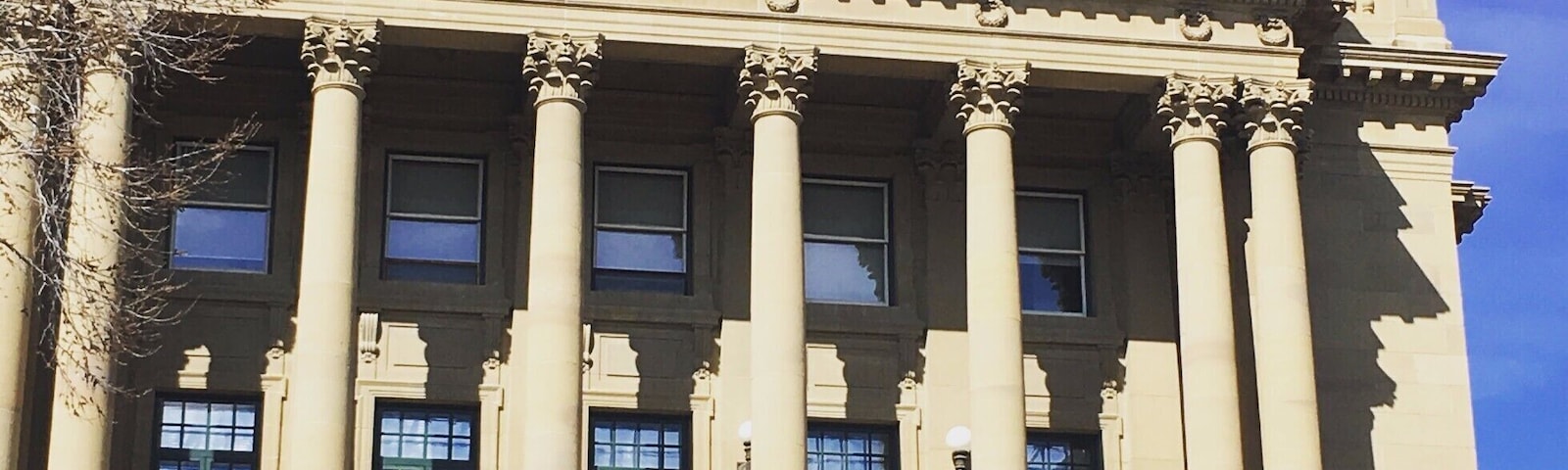 Un grand bâtiment de style néoclassique, doté de colonnes, de fenêtres en arc de cercle et d’un drapeau.