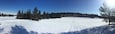 A snowy landscape with a clear blue sky, a forest of evergreen trees, and a frozen lake.