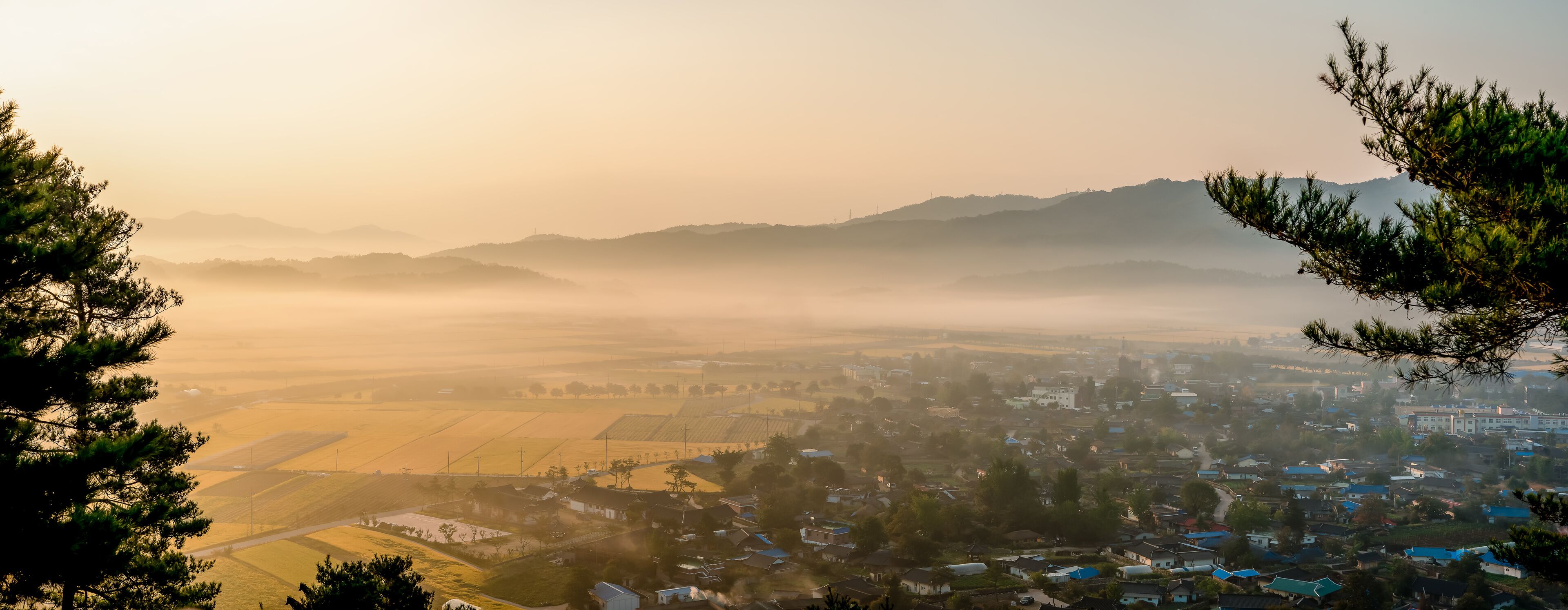 A misty valley with fields, houses, and distant mountains.