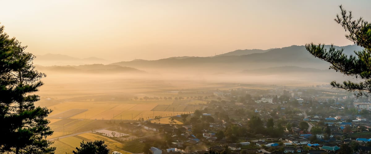 A misty valley with fields, houses, and distant mountains.