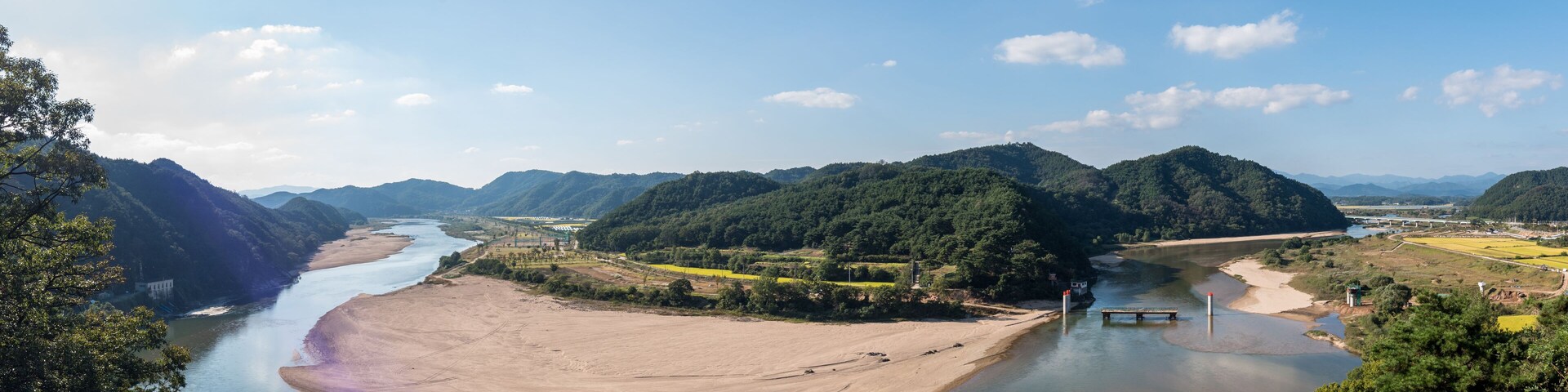 Un río serpentea por un valle flanqueado por montañas y un puente a lo lejos.