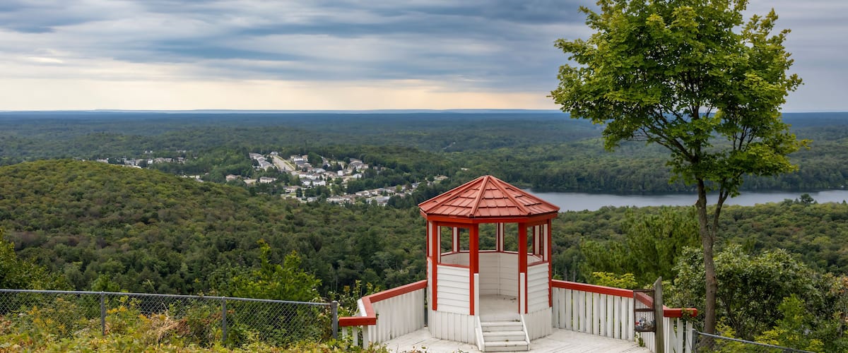 A gazebo overlooking a forested valley with a lake and distant houses.