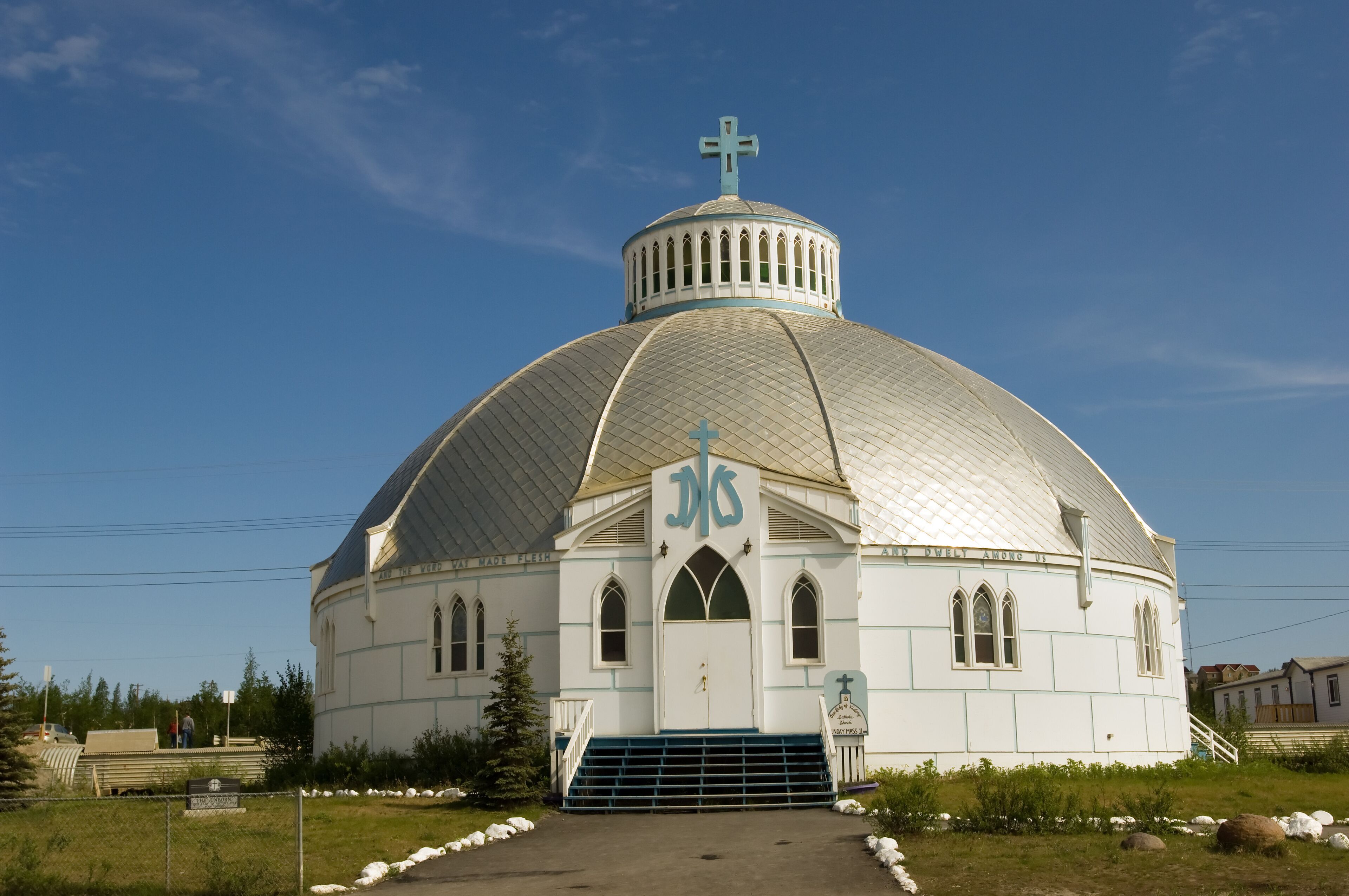A white church with a dome and cross, surrounded by grass and rocks.