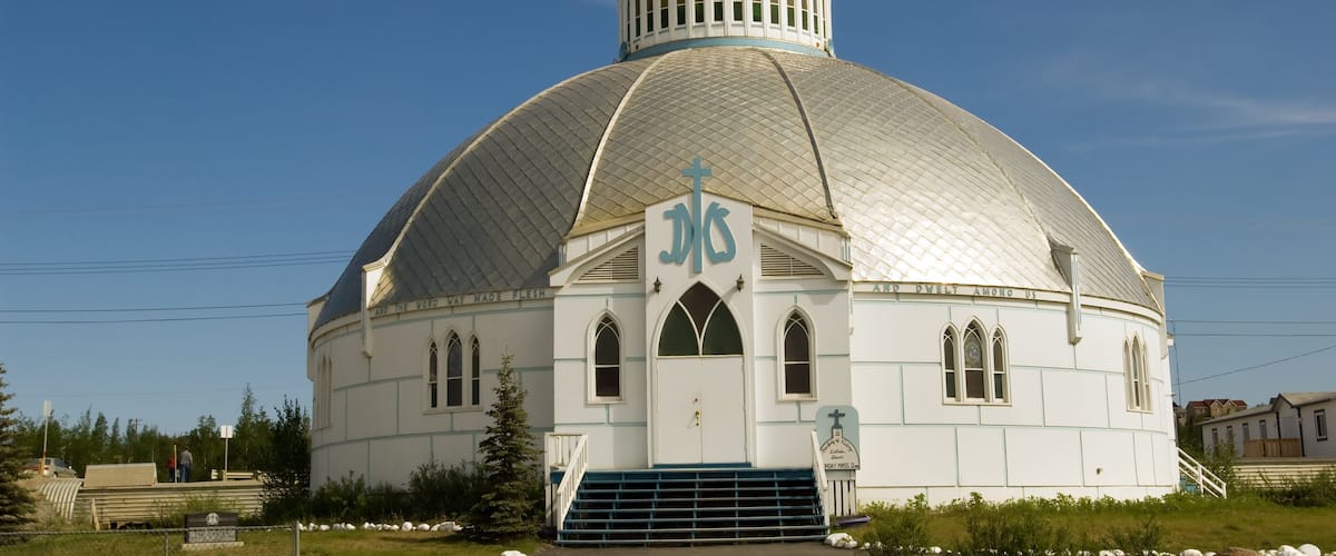 A white church with a dome and cross, surrounded by grass and rocks.