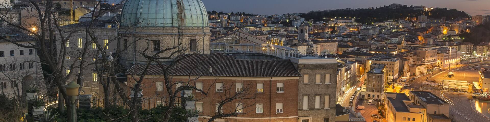 A cityscape at dusk with a prominent dome structure, a winding road, and surrounding buildings.