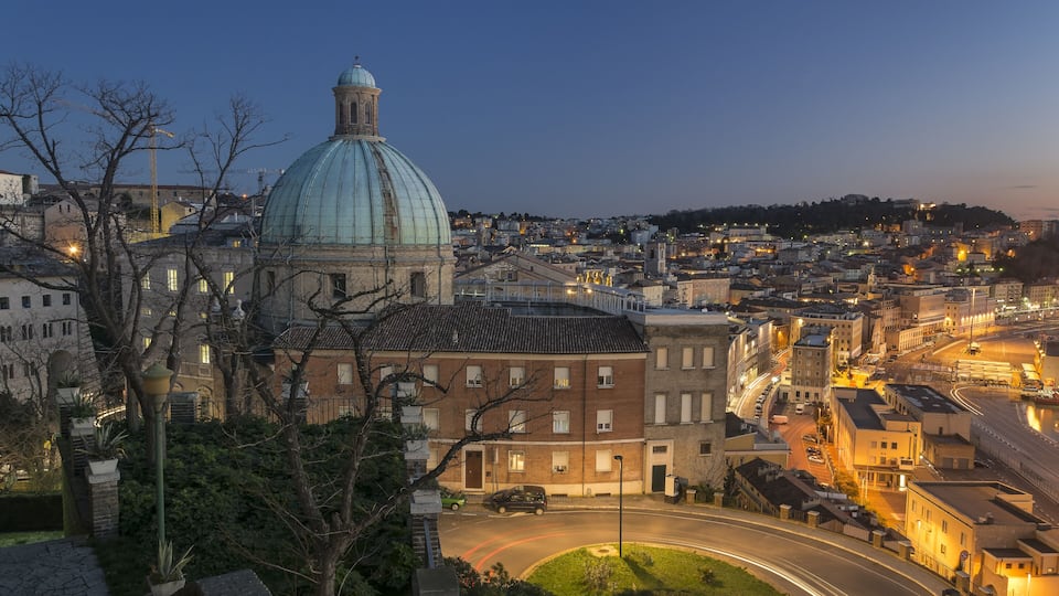 A cityscape at dusk with a prominent dome structure, a winding road, and surrounding buildings.