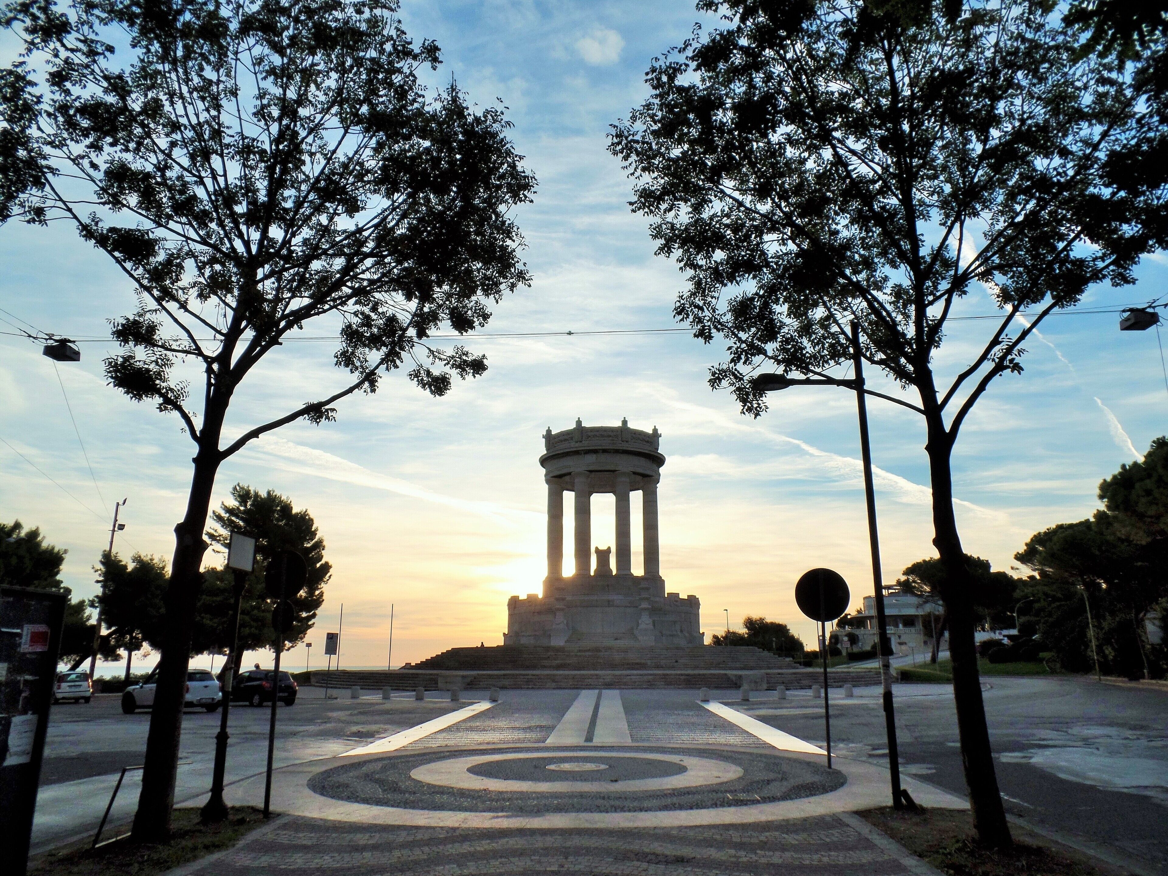 A monument with columns, surrounded by trees and a circular pattern on the ground.