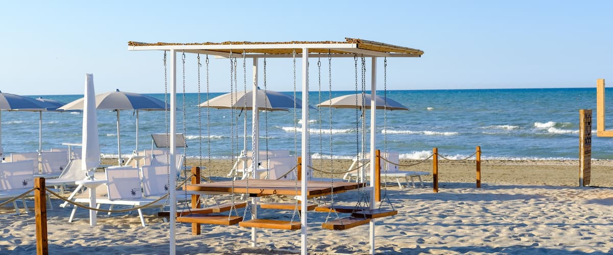 A beach with a wooden swing structure, white lounge chairs, and umbrellas.