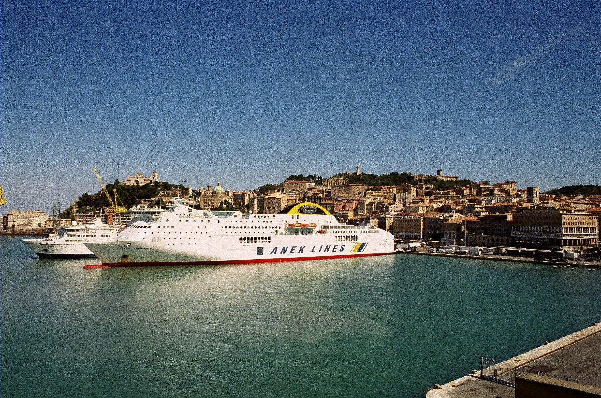 A large cruise ship docked at a port with a cityscape in the background.