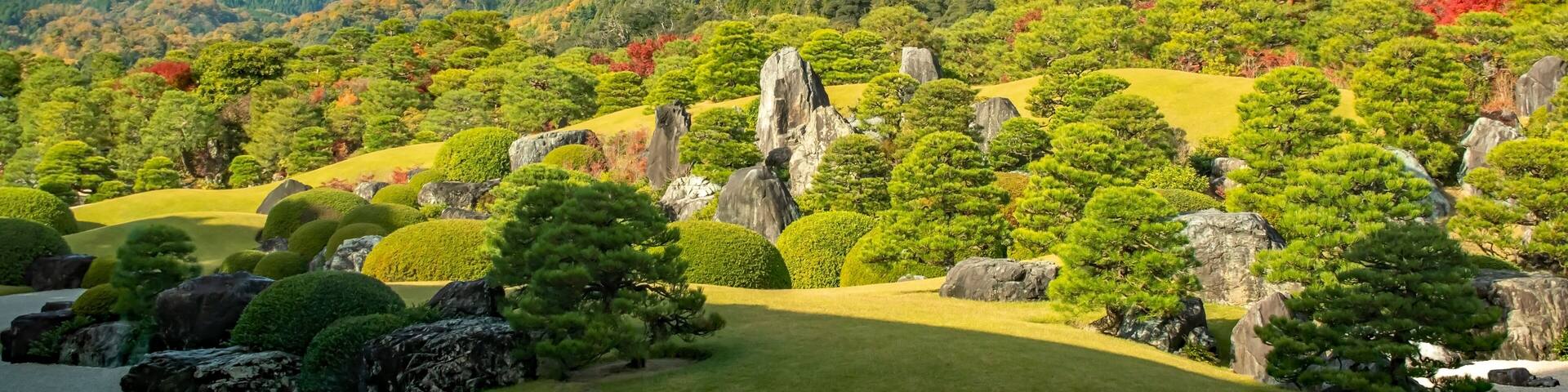 A landscaped garden with neatly trimmed trees, rocks, and a hill in the background.