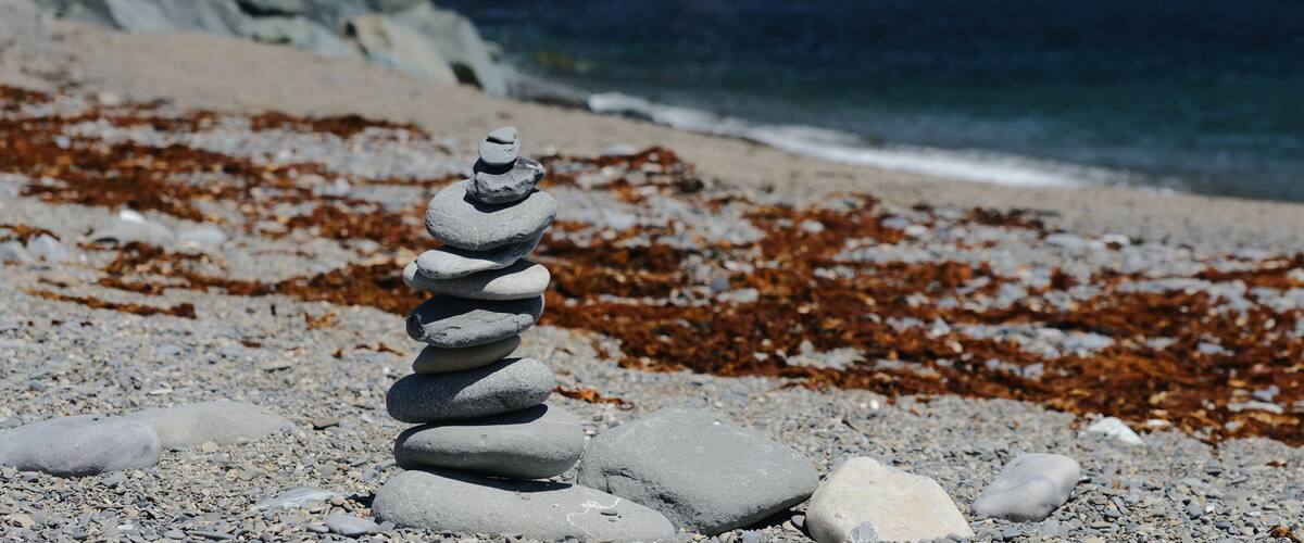 A stack of stones on a pebbly beach with seaweed in the background.