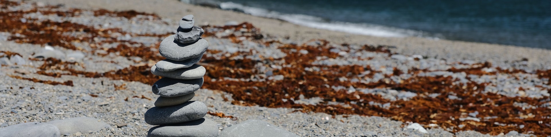A stack of stones on a pebbly beach with seaweed in the background.