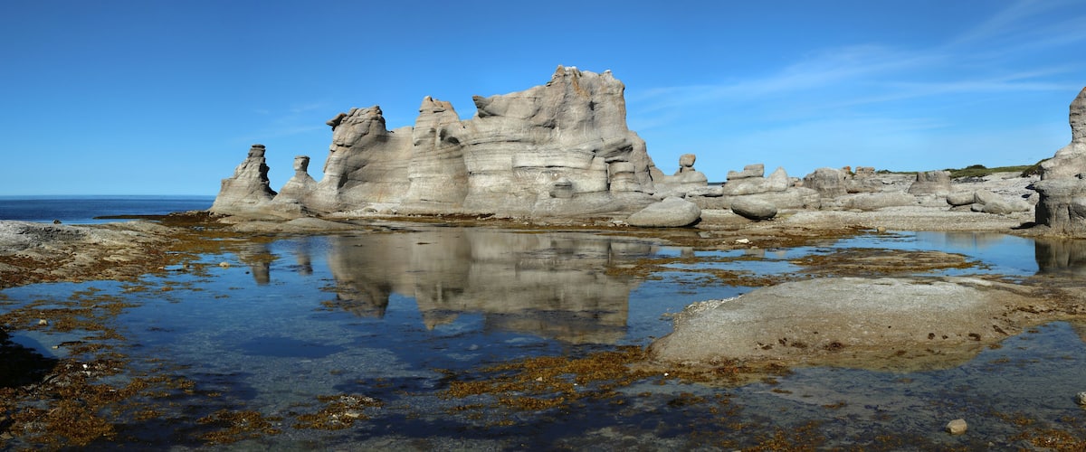 A coastal landscape with unique rock formations and a reflective water surface.