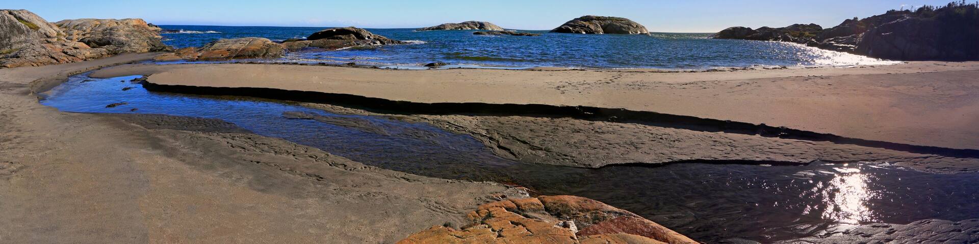 A coastal beach with rocky outcrops and calm waters.