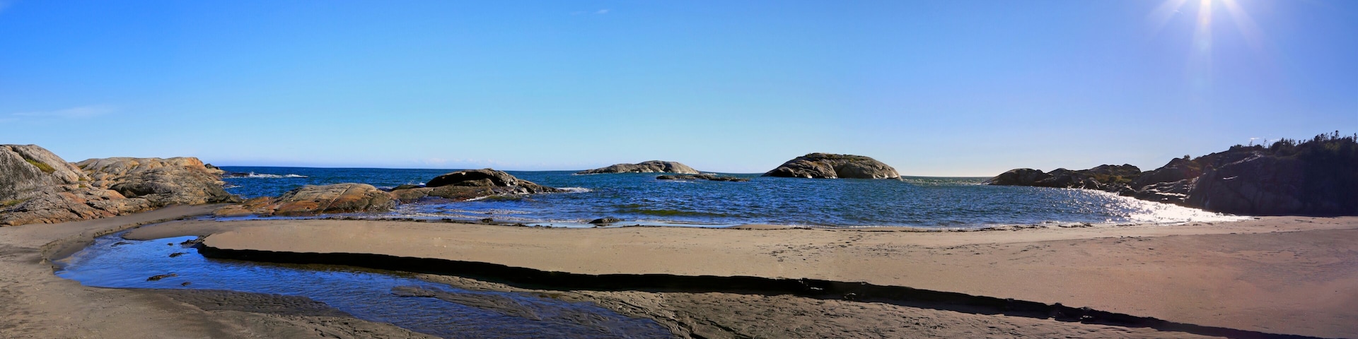 A coastal beach with rocky outcrops and calm waters.