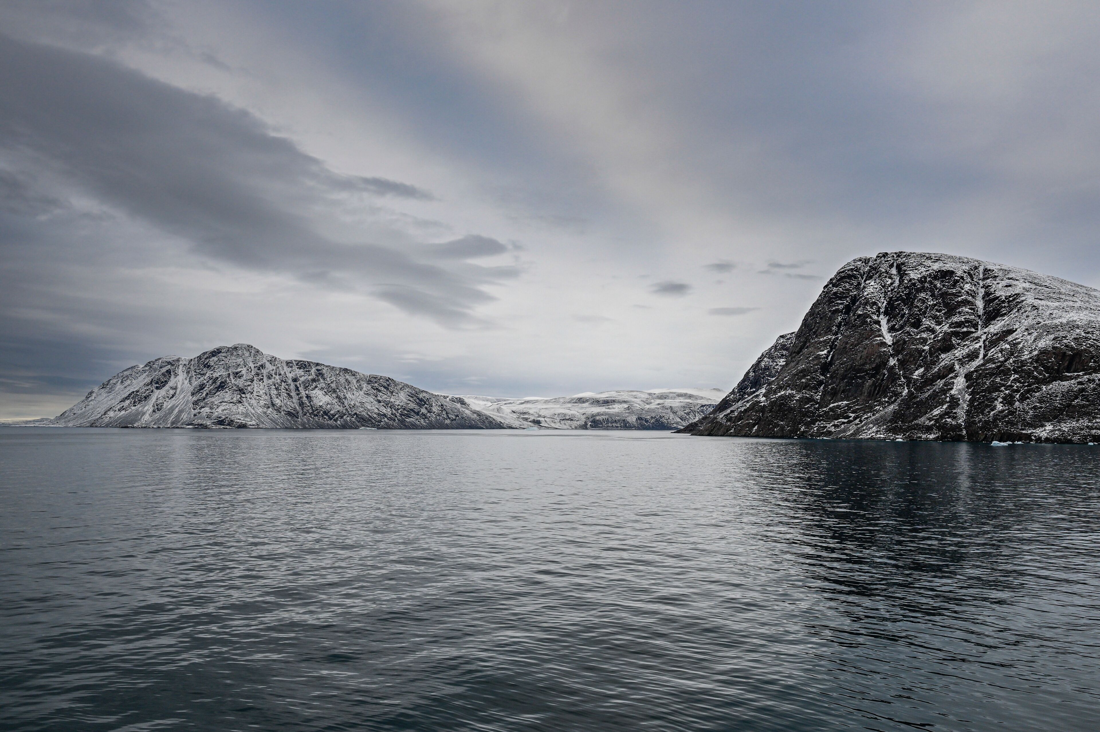 A calm fjord with snow-covered mountains and a cloudy sky.