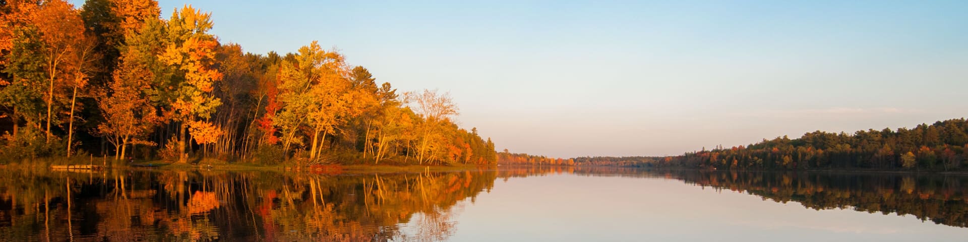 Northern Ontario lake at sundown on a late summer's day. Mirror-like reflections and glowing orange forest.