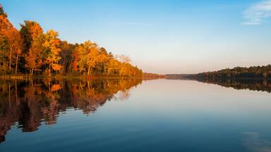 Northern Ontario lake at sundown on a late summer's day. Mirror-like reflections and glowing orange forest.