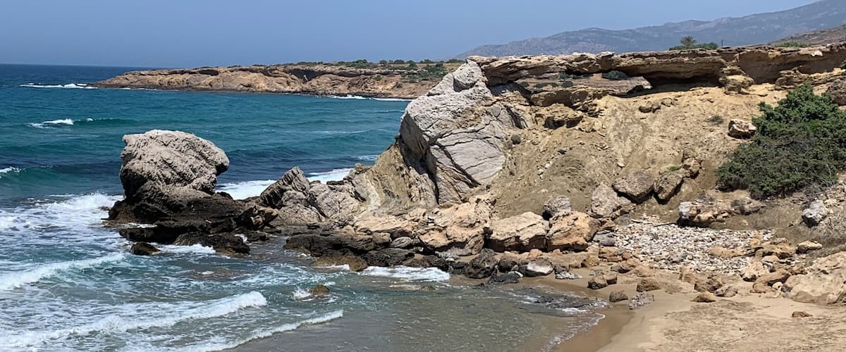 A rocky coastline with clear blue waters and a sandy beach.