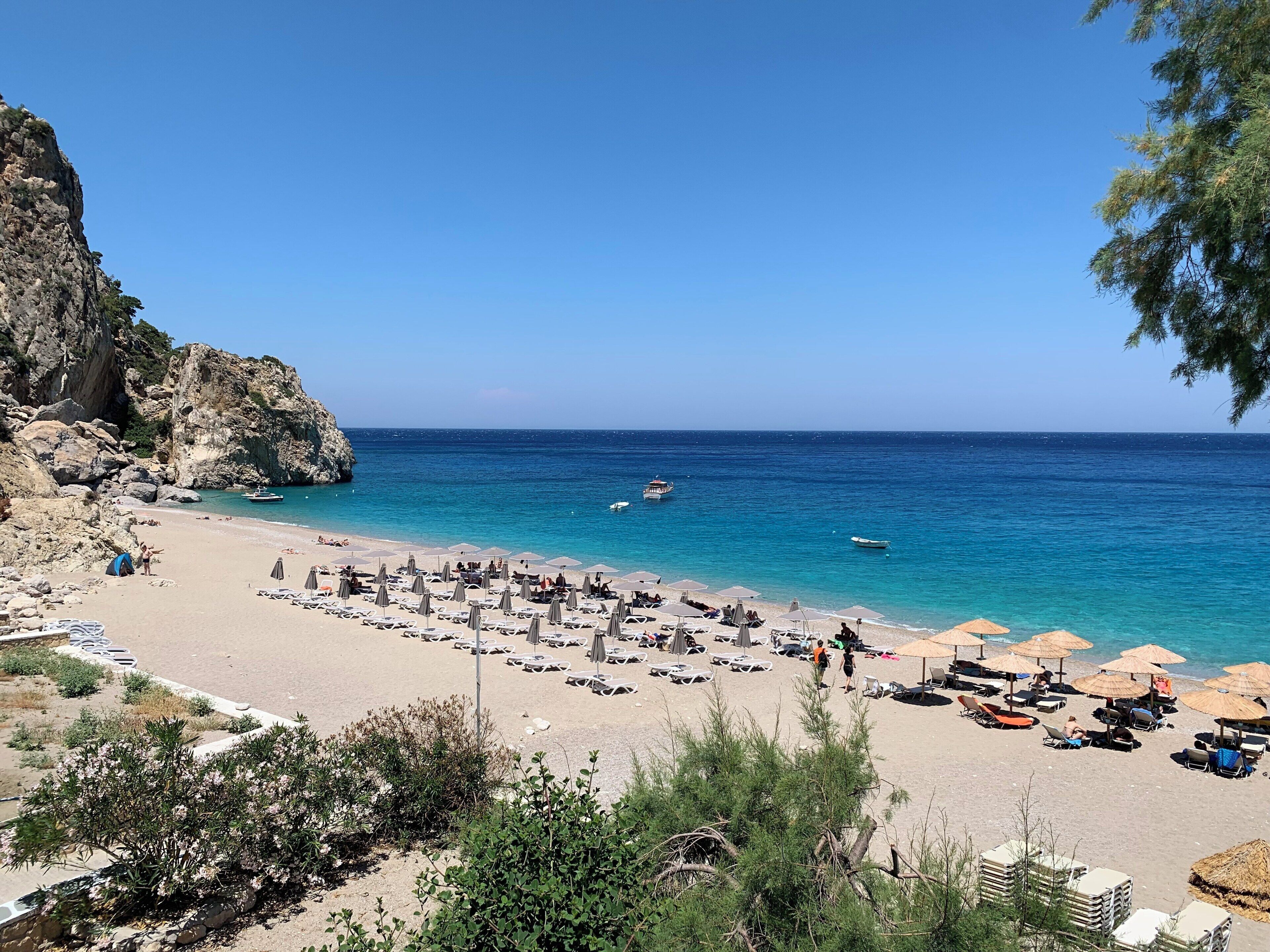 A beach with clear blue water, rocky cliffs, and umbrellas.