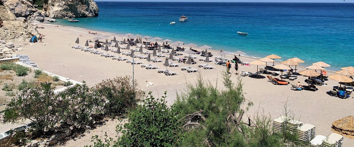 A beach with clear blue water, rocky cliffs, and umbrellas.