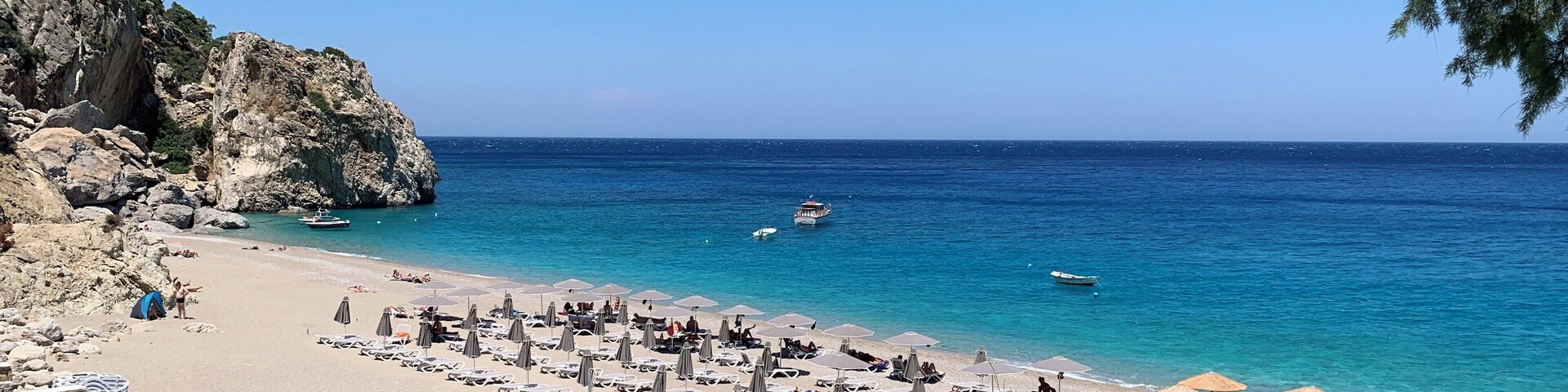 A beach with clear blue water, rocky cliffs, and umbrellas.